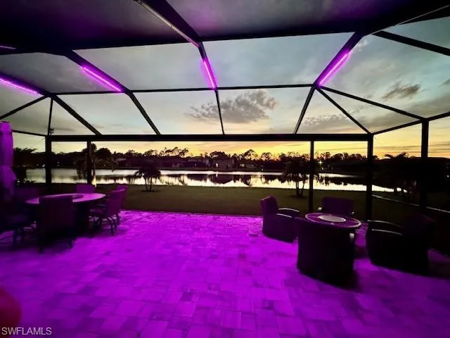 Patio terrace at dusk featuring glass enclosure and a water view