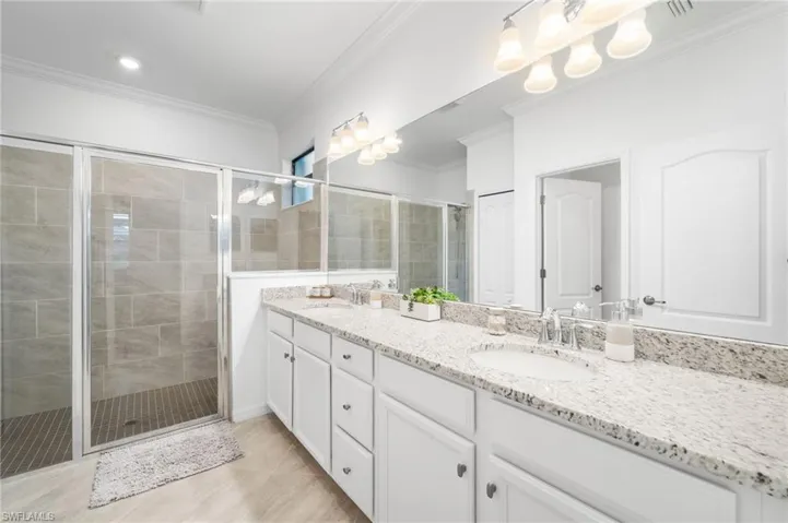 Bathroom with tile patterned flooring, double vanity, crown molding, and a shower with shower door