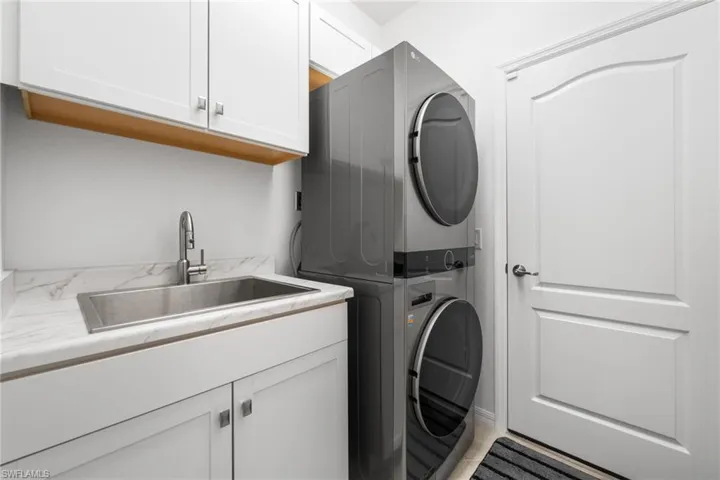Washroom featuring sink, stacked washer and dryer, and cabinets