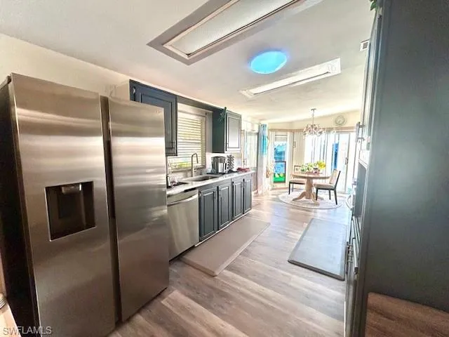 Kitchen featuring stainless steel appliances, light wood finished floors, light countertops, hanging light fixtures, and a chandelier