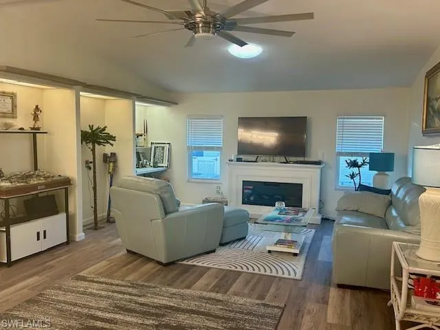 Living area featuring wood finished floors, vaulted ceiling, a glass covered fireplace, and ceiling fan