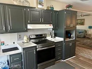 Kitchen with electric stove, light countertops, under cabinet range hood, light wood-type flooring, and gray cabinets