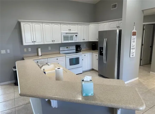 Kitchen with light tile patterned flooring, white cabinets, white appliances, and a breakfast bar