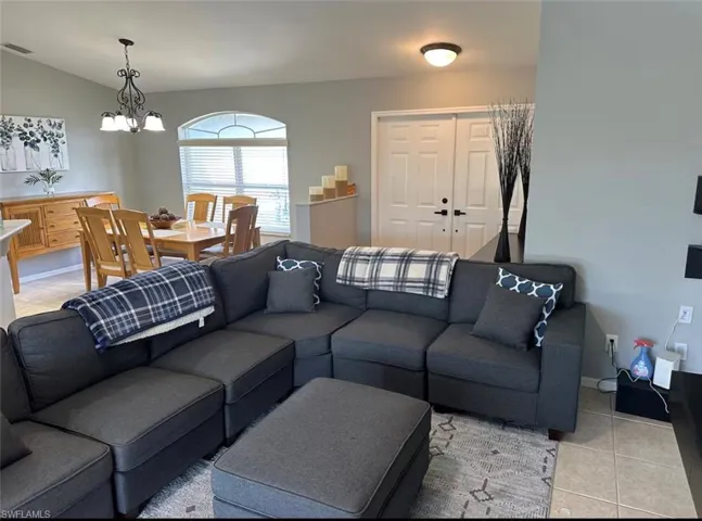 Living room featuring suspended lighting, light tile patterned flooring, and vaulted ceiling