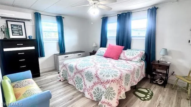 Bedroom featuring light wood finished floors, a wall mounted AC, multiple windows, and ceiling fan