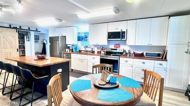 Kitchen featuring a barn door, butcher block countertops, a breakfast bar, appliances with stainless steel finishes, and white cabinetry