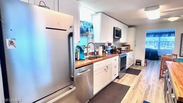 Kitchen featuring stainless steel appliances, butcher block countertops, white cabinetry, and light wood-type flooring