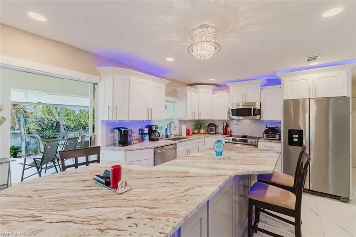 Kitchen featuring stainless steel appliances, a breakfast bar area, light stone countertops, white cabinets, and hanging lights
