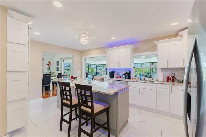 Two tone kitchen featuring a center island, stainless steel fridge, a kitchen breakfast bar, light stone counters, and light marble finish flooring
