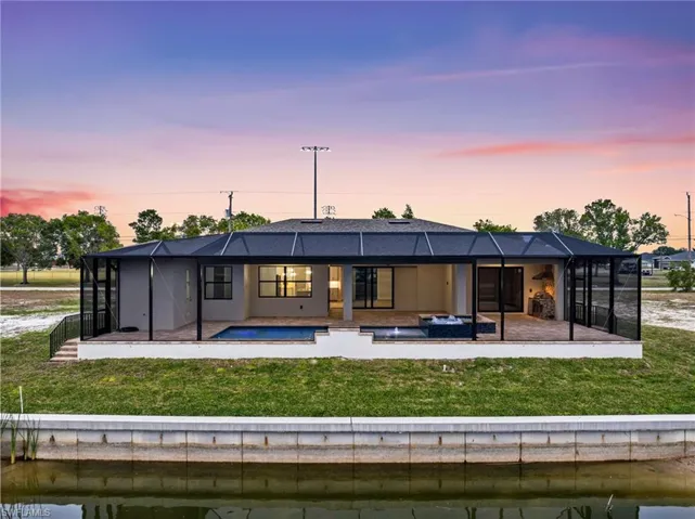 Back house at dusk featuring a lawn, glass enclosure, and a patio