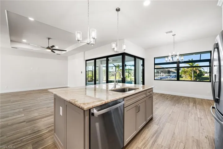 Kitchen featuring light stone countertops, stainless steel appliances, sink, gray cabinets, and an island with sink