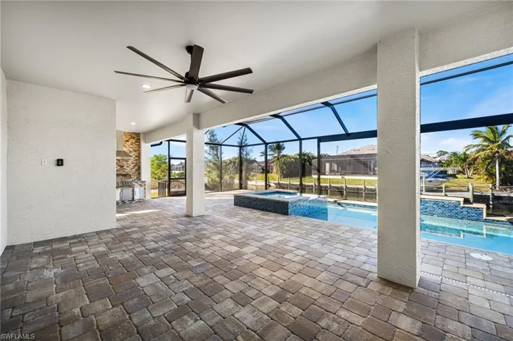 View of swimming pool featuring glass enclosure, ceiling fan, exterior kitchen, a patio area, and an in ground hot tub