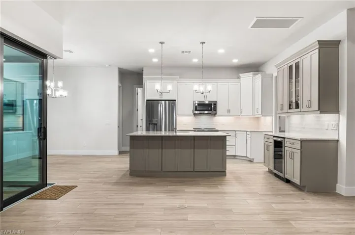 Kitchen with appliances with stainless steel finishes, gray cabinetry, pendant lighting, and a kitchen island