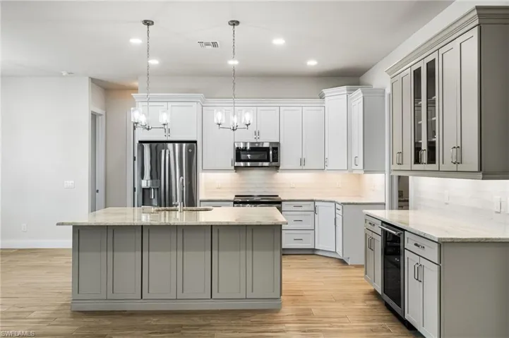 Kitchen with gray cabinetry, a center island with sink, stainless steel appliances, and wine cooler