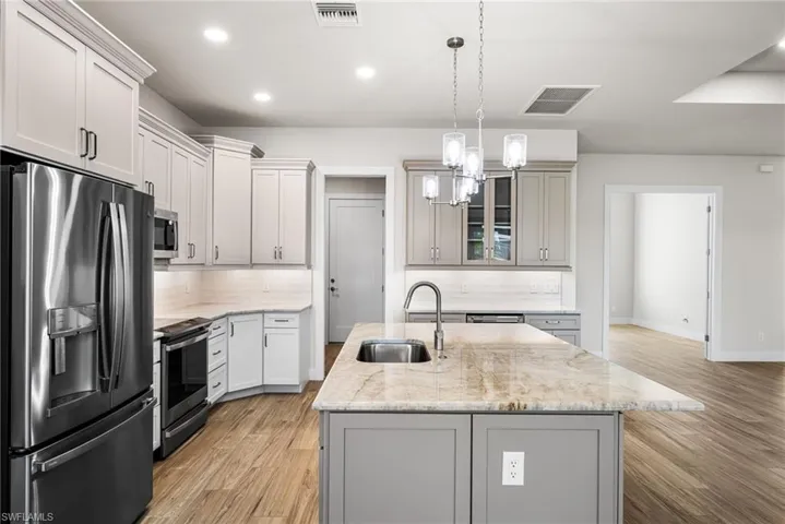 Kitchen with sink, a kitchen island with sink, stainless steel appliances, light stone counters, and decorative backsplash