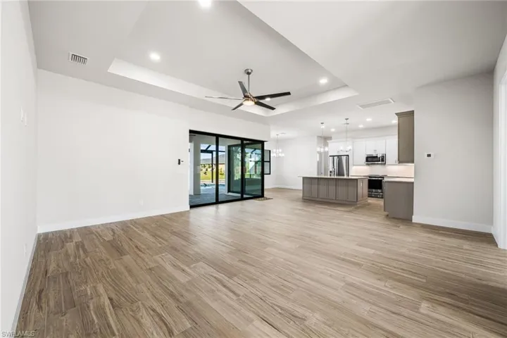 Unfurnished living room with ceiling fan, a raised ceiling, and light wood-type flooring
