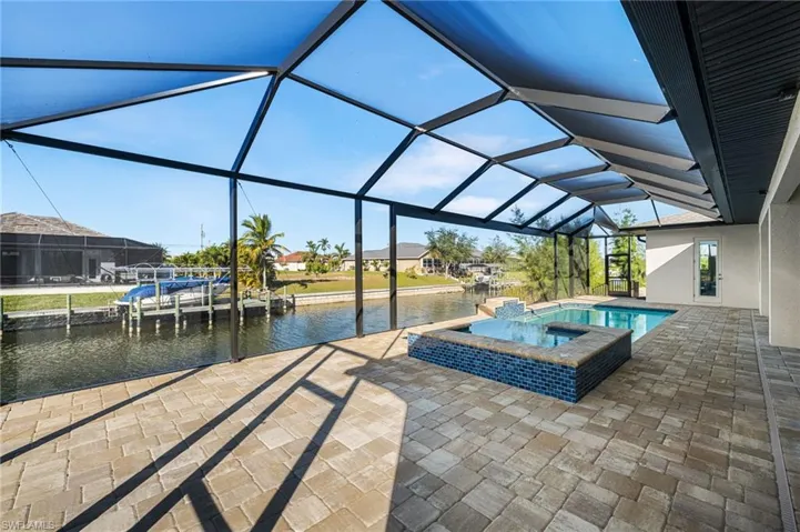 View of swimming pool featuring an in ground hot tub, a water view, glass enclosure, and a patio area