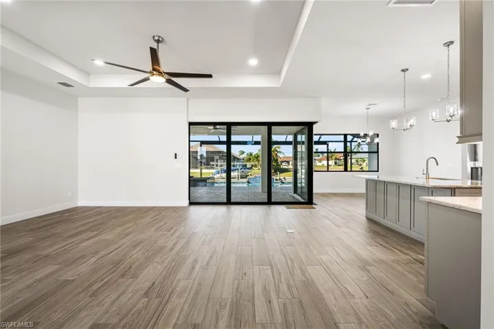 Unfurnished living room featuring a tray ceiling, sink, ceiling fan with notable chandelier, and light hardwood / wood-style flooring