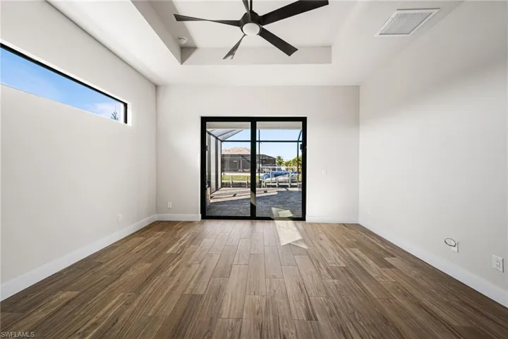 Unfurnished room with dark hardwood / wood-style flooring, a raised ceiling, ceiling fan, and a healthy amount of sunlight