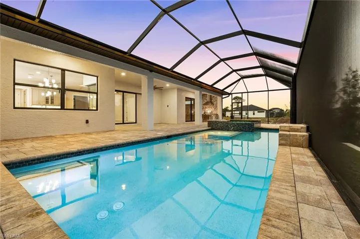 Pool at dusk with a patio, glass enclosure, and an in ground hot tub