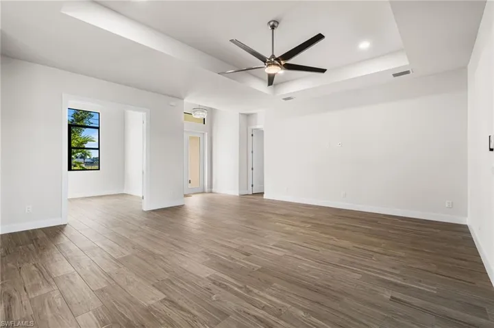 Unfurnished room with hardwood / wood-style flooring, ceiling fan, and a raised ceiling