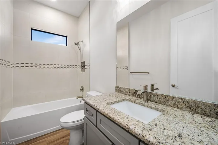 Full bathroom with hardwood / wood-style floors, vanity, toilet, and tiled shower / bath combo