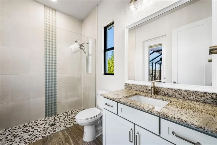 Bathroom featuring tiled shower, vanity, hardwood / wood-style flooring, and toilet