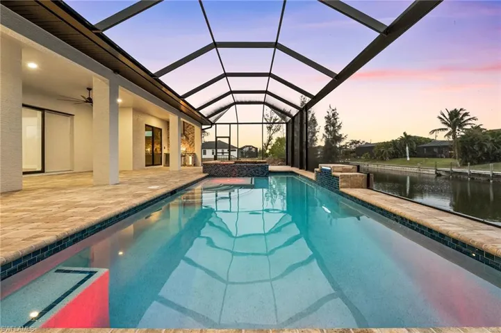 Pool at dusk featuring glass enclosure, a patio area, a water view, and ceiling fan