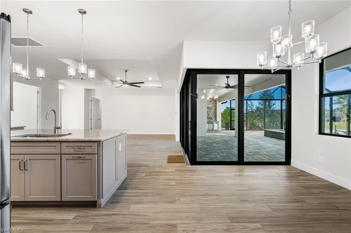 Kitchen with gray cabinets, sink, light stone countertops, and hanging light fixtures
