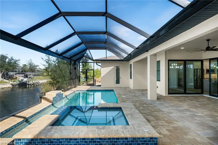 View of pool with an in ground hot tub, a water view, ceiling fan, and a lanai