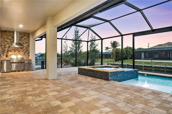 Pool at dusk with grilling area, glass enclosure, a patio area, exterior kitchen, and an in ground hot tub