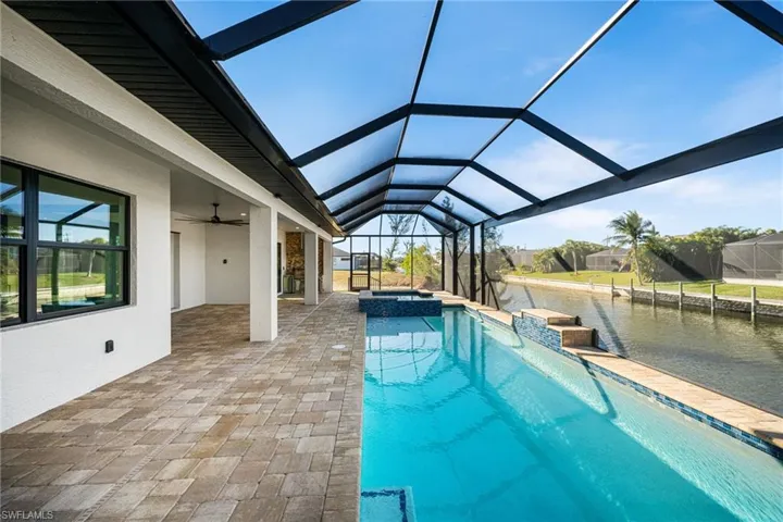 View of swimming pool featuring a lanai, a patio area, an in ground hot tub, and a water view