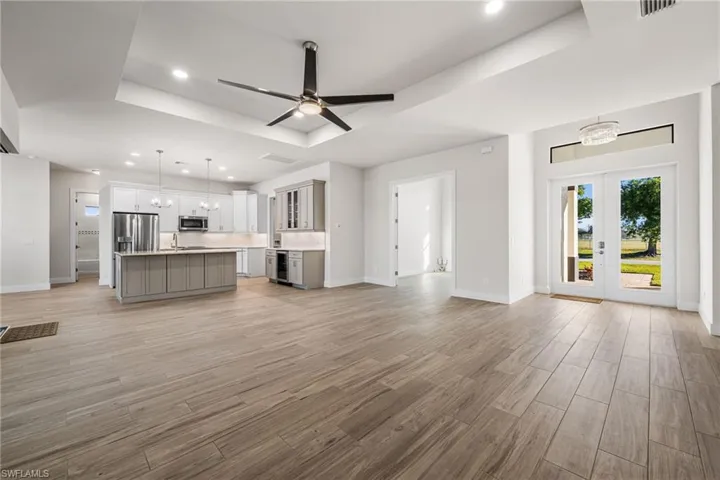Unfurnished living room featuring french doors, ceiling fan with notable chandelier, sink, a tray ceiling, and beverage cooler