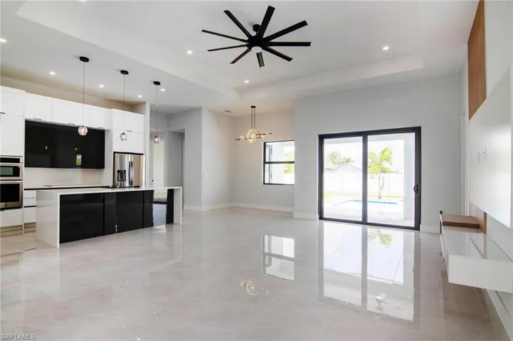 Kitchen featuring pendant lighting, a raised ceiling, a large island with sink, stainless steel appliances, and white cabinetry