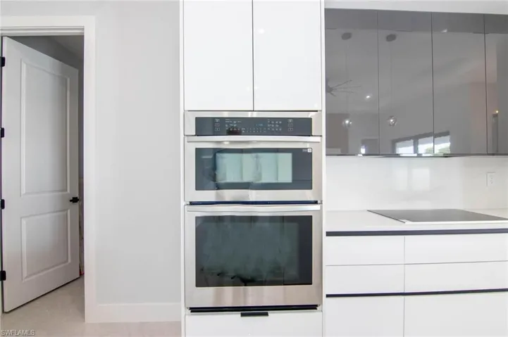 Kitchen with black electric cooktop, white cabinets, stainless steel double oven, and light tile patterned flooring