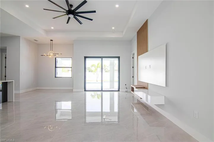 Unfurnished living room with a raised ceiling and ceiling fan with notable chandelier