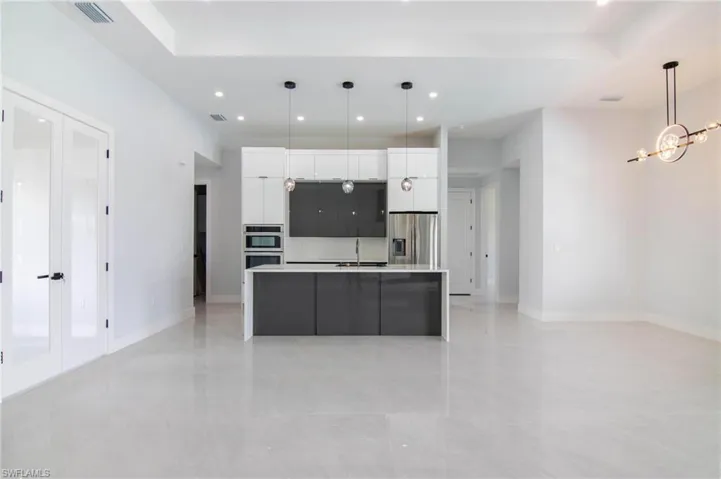 Kitchen featuring an island with sink, stainless steel appliances, white cabinets, pendant lighting, and a notable chandelier