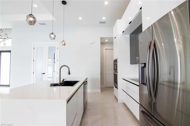 Kitchen featuring white cabinets, hanging light fixtures, sink, and stainless steel refrigerator with ice dispenser