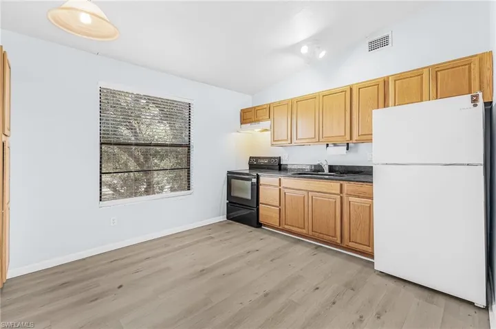 Kitchen space featuring light wood-finish cabinetry, dark countertops, and wood-finish flooring