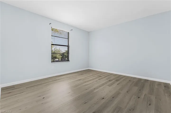 Spacious room featuring light wood-finish flooring, light blue wall paint, white baseboards, and a window with horizontal blinds