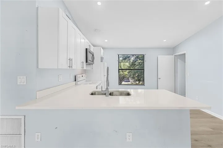 Spacious kitchen featuring an extended white countertop with an undermount double-basin sink, modern stainless-steel faucet, white shaker-style cabinetry, and wood-finish flooring