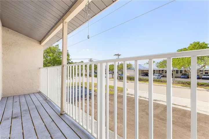 Covered balcony featuring wood-finish flooring, stucco exterior wall, and white vertical baluster railing