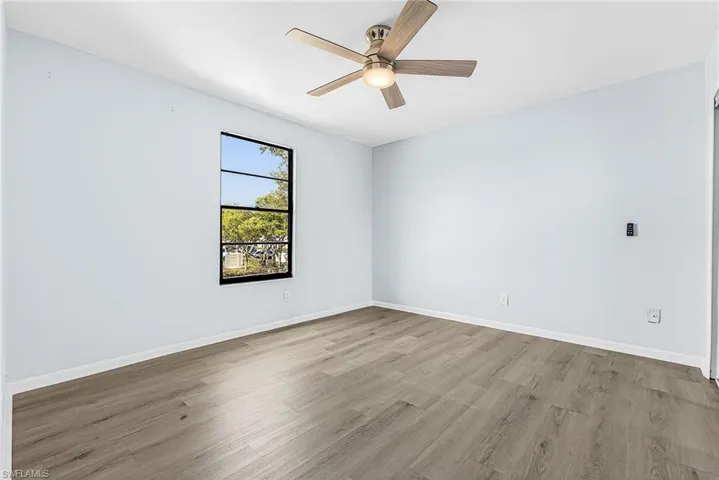 Spacious room featuring light blue walls, wood-finish flooring, a ceiling fan with integrated lighting, and a multi-pane window