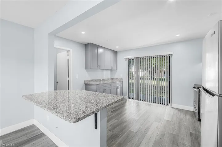 Kitchen featuring a breakfast bar with stone countertop, stainless steel appliances, recessed lighting, wood-finish flooring, and sliding glass doors