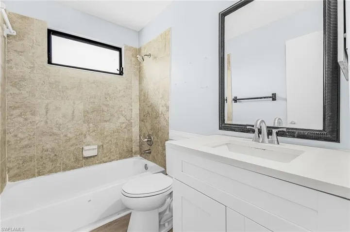Bathroom featuring a white vanity with a rectangular undermount sink, a large framed mirror, and a full-size bathtub with tiled walls and a shower fixture