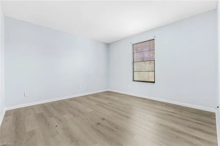 Room featuring wood-finish flooring, light blue wall paint, white baseboards, and a window with a dark frame