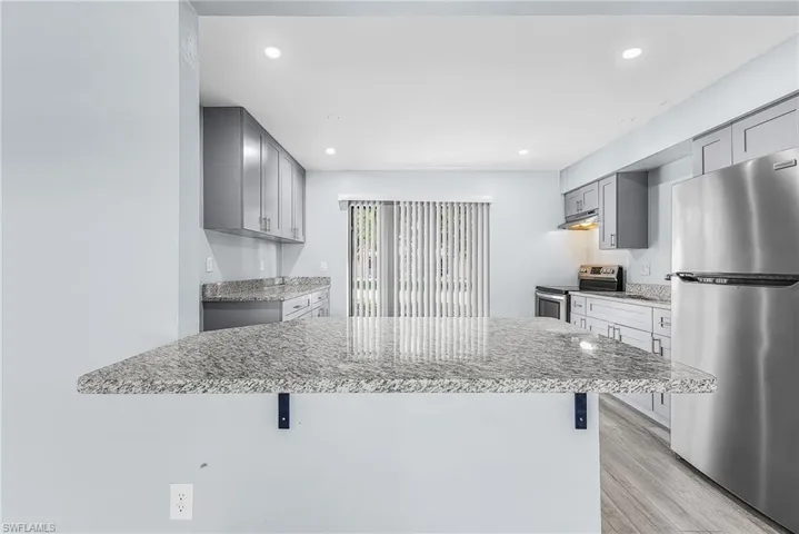 Kitchen featuring light gray cabinetry, stainless steel appliances, granite countertops, wood-finish flooring, and recessed lighting