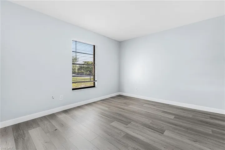 Room featuring light blue walls, wood-finish flooring, white baseboards, and a window with horizontal blinds