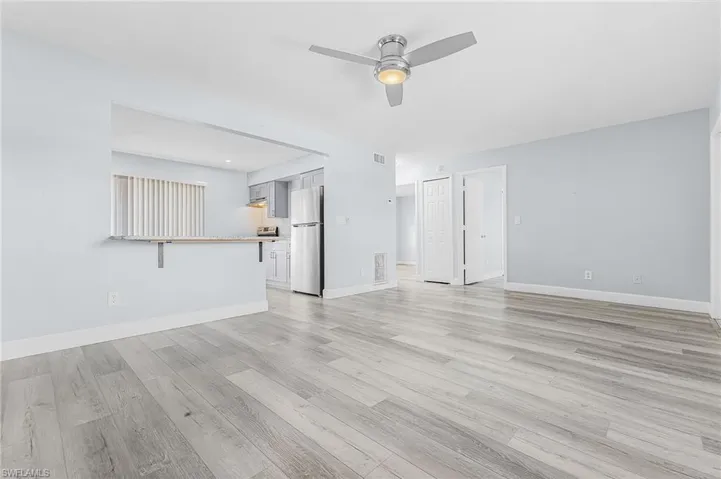 Open-concept living space featuring wood-finish flooring, a contemporary ceiling fan, and a pass-through bar to the kitchen with light gray cabinetry and stainless steel appliances