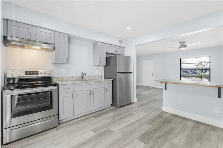 Contemporary kitchen featuring grey shaker-style cabinetry, stainless steel appliances, granite countertops, wood-finish flooring, and a breakfast bar